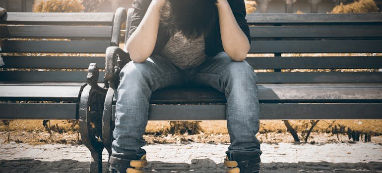 young man sitting on a bench and holding his head experiencing social anxiety disorder symptoms.